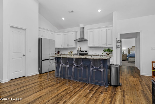 kitchen with visible vents, white cabinets, light stone counters, freestanding refrigerator, and wall chimney range hood