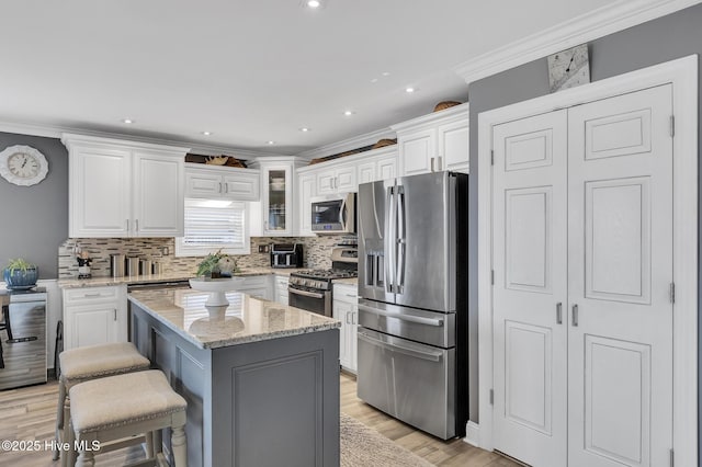 kitchen with a breakfast bar area, appliances with stainless steel finishes, white cabinets, a kitchen island, and light stone counters