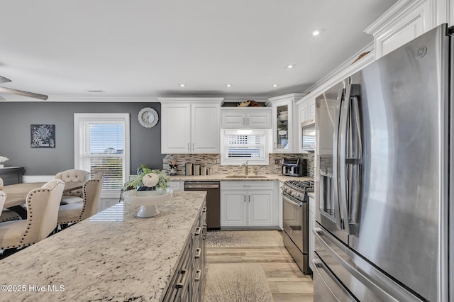 kitchen with white cabinetry, stainless steel appliances, sink, backsplash, and light stone counters