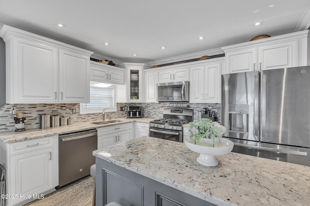 kitchen with white cabinets, appliances with stainless steel finishes, decorative backsplash, sink, and light stone counters