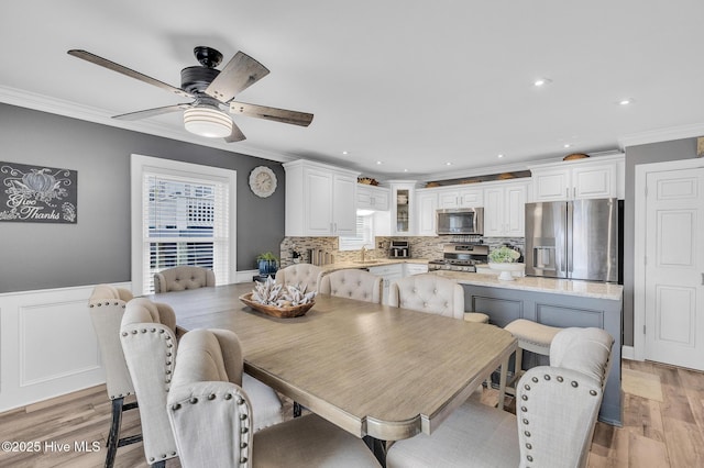 dining space with ceiling fan, light wood-type flooring, sink, and crown molding