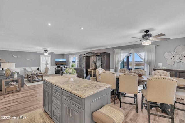 kitchen with a kitchen island, light hardwood / wood-style floors, ceiling fan, gray cabinets, and light stone counters