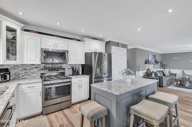 kitchen featuring tasteful backsplash, white cabinetry, appliances with stainless steel finishes, a breakfast bar area, and light stone counters