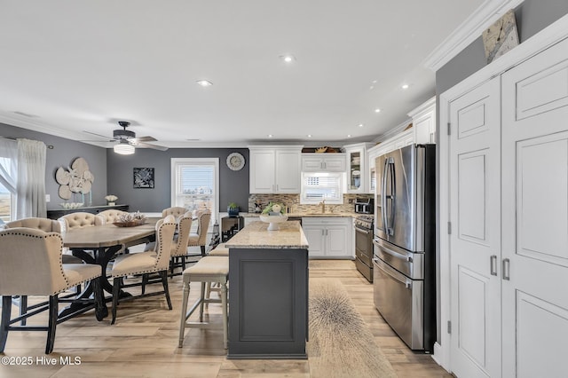 kitchen featuring backsplash, a kitchen island, white cabinetry, light stone countertops, and appliances with stainless steel finishes