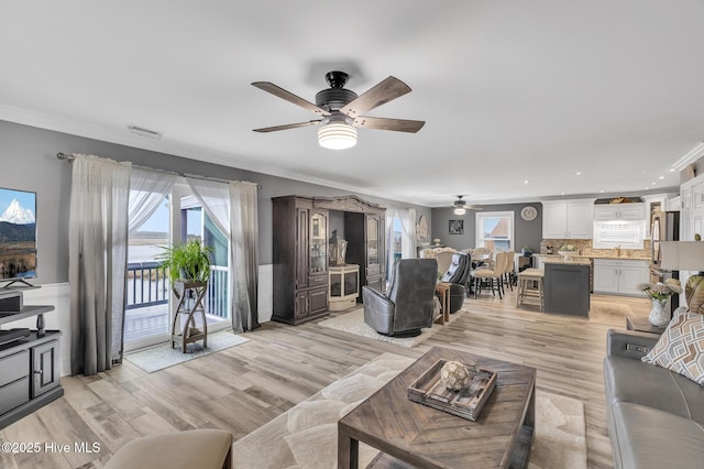 living room featuring ceiling fan, sink, crown molding, and light wood-type flooring