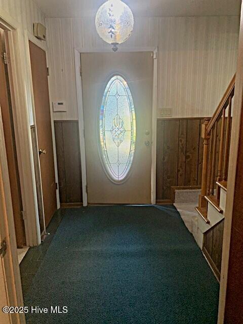 entryway with wood walls and dark colored carpet