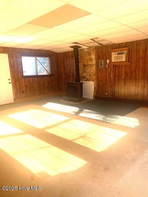 interior space with a paneled ceiling, an AC wall unit, wood walls, and a wood stove