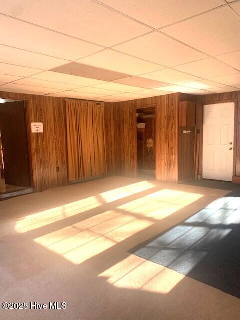 carpeted spare room with a drop ceiling and wood walls