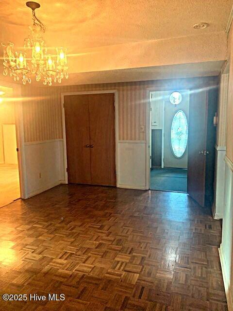 foyer entrance with dark parquet flooring, an inviting chandelier, and a textured ceiling