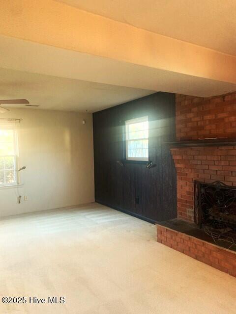 unfurnished living room with a brick fireplace, a wealth of natural light, and carpet floors