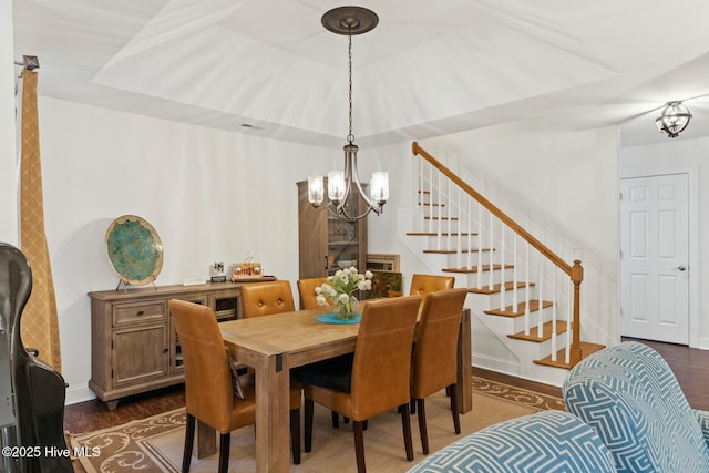 dining area featuring dark wood-type flooring, a tray ceiling, and an inviting chandelier