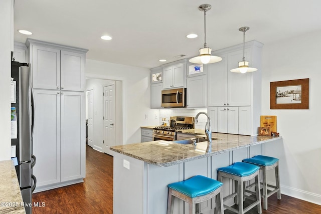 kitchen with sink, light stone counters, decorative light fixtures, appliances with stainless steel finishes, and kitchen peninsula