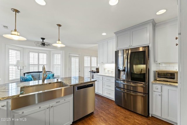 kitchen with sink, appliances with stainless steel finishes, white cabinetry, hanging light fixtures, and light stone counters