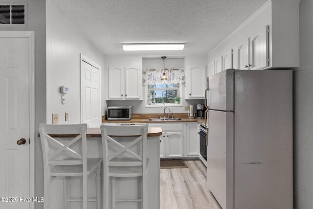 1503 Carolina Beach Ave N Unit 1D, Carolina Beach, NC 28428 - kitchen featuring freestanding refrigerator, stainless steel microwave, a textured ceiling, a sink, and white cabinets