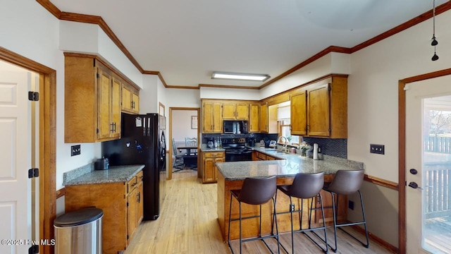 kitchen with a breakfast bar, black appliances, sink, light hardwood / wood-style floors, and kitchen peninsula
