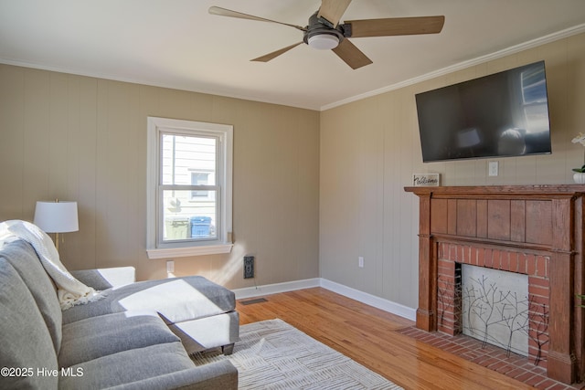 living room with a brick fireplace, crown molding, light hardwood / wood-style floors, and ceiling fan