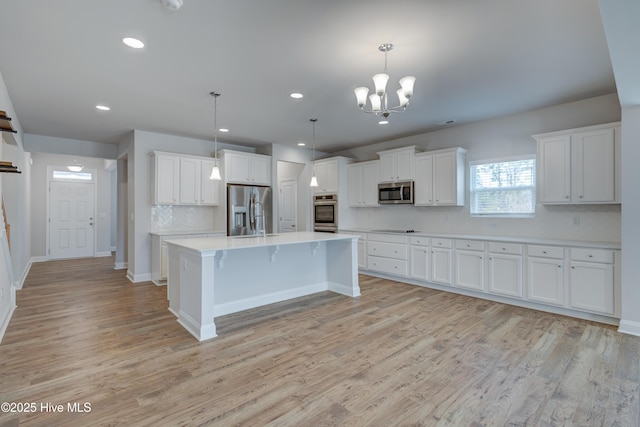 kitchen with white cabinets, appliances with stainless steel finishes, light countertops, light wood-style floors, and pendant lighting