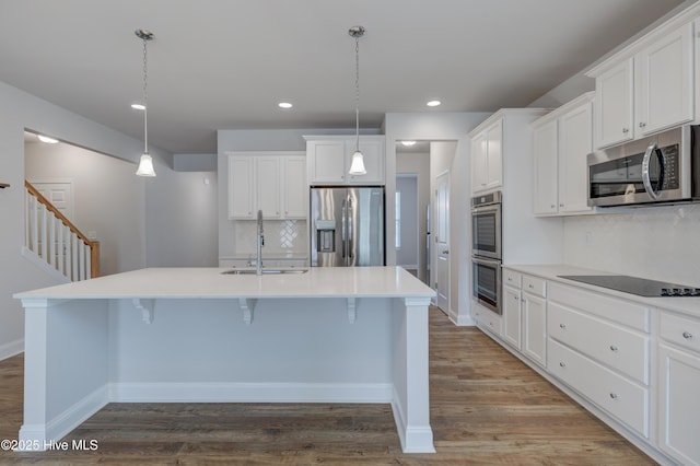 kitchen with wood finished floors, a sink, white cabinets, appliances with stainless steel finishes, and an island with sink