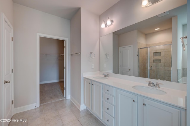 bathroom with double vanity, a shower stall, a walk in closet, and a sink