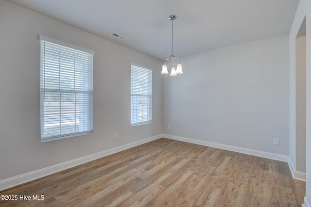 empty room with visible vents, a notable chandelier, light wood-style flooring, and baseboards