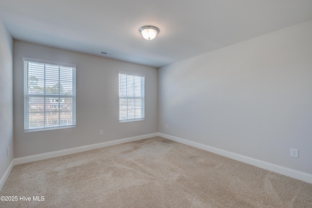 spare room featuring light carpet, visible vents, and baseboards