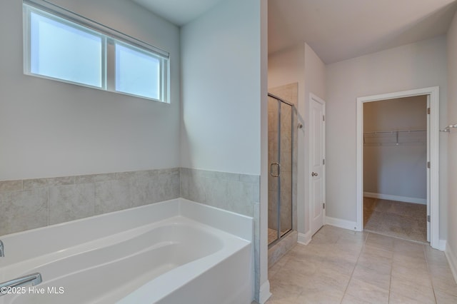 full bath featuring a walk in closet, a garden tub, a shower stall, baseboards, and tile patterned floors