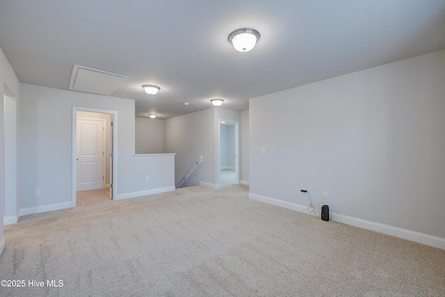 spare room featuring light carpet, attic access, and baseboards