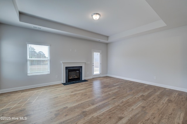 unfurnished living room with baseboards, visible vents, a raised ceiling, and wood finished floors