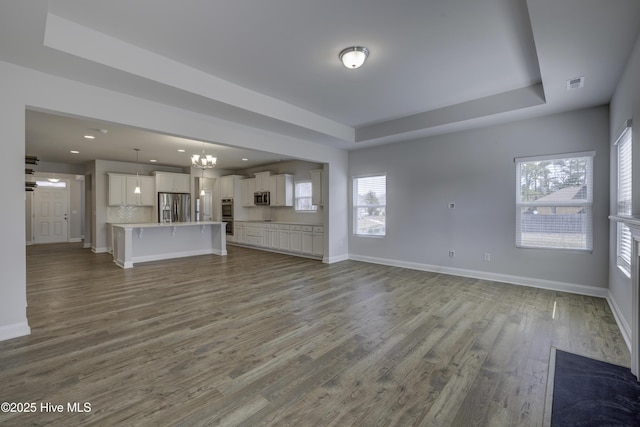 unfurnished living room with baseboards, visible vents, a raised ceiling, and wood finished floors