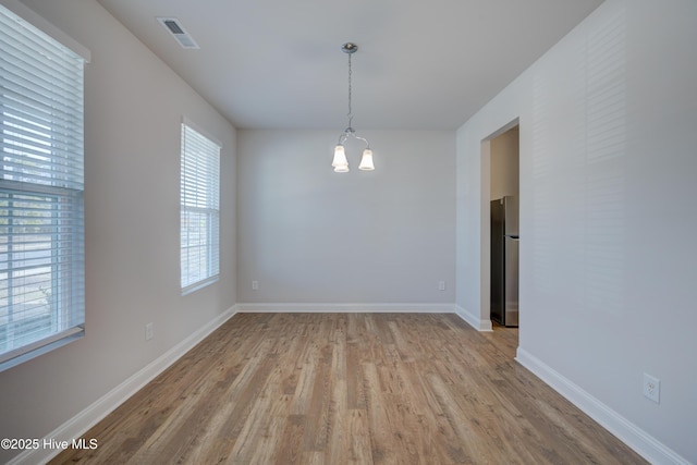 empty room featuring baseboards, wood finished floors, visible vents, and a notable chandelier