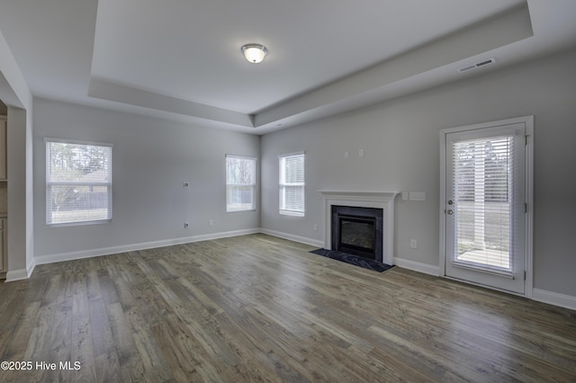 unfurnished living room featuring a raised ceiling, visible vents, a fireplace with flush hearth, wood finished floors, and baseboards