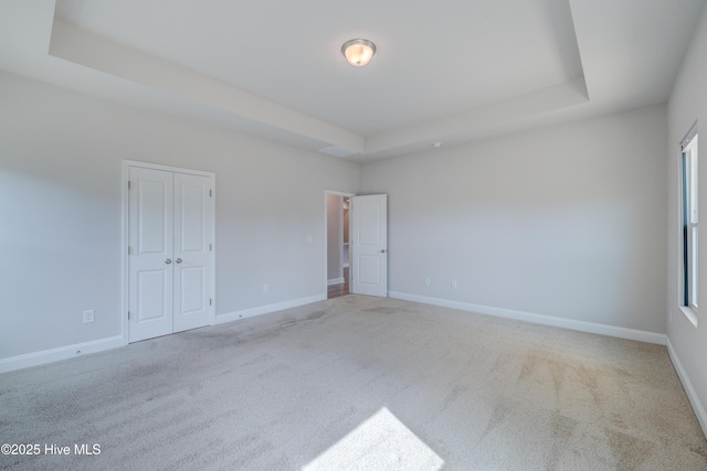 carpeted empty room featuring baseboards and a raised ceiling