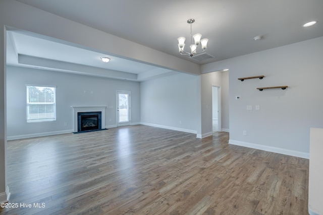 unfurnished living room featuring a chandelier, baseboards, and wood finished floors