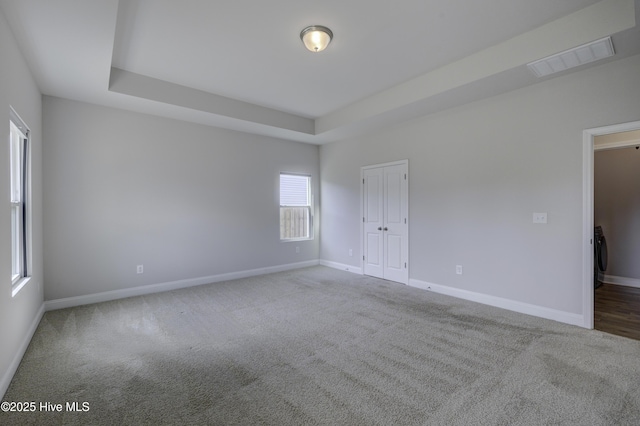 carpeted empty room with a raised ceiling, visible vents, and baseboards