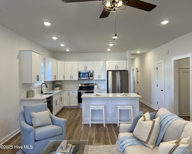 kitchen with white cabinetry, stainless steel appliances, backsplash, a kitchen island, and sink