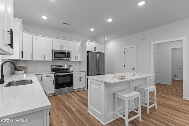 kitchen featuring stainless steel appliances, a breakfast bar, a sink, and white cabinetry