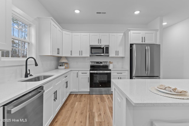 kitchen with wood finished floors, a healthy amount of sunlight, stainless steel dishwasher, white cabinetry, and a sink