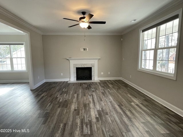 unfurnished living room with dark wood-type flooring, a high end fireplace, ornamental molding, and ceiling fan