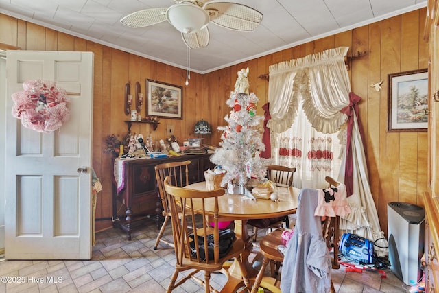 dining space featuring ceiling fan, wooden walls, and crown molding