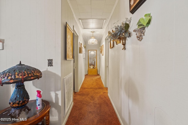 corridor with crown molding, a notable chandelier, and carpet flooring