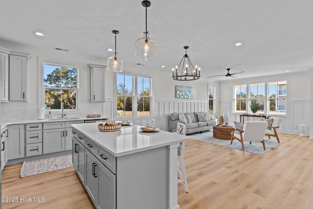 living room with ornamental molding, sink, ceiling fan with notable chandelier, and light hardwood / wood-style flooring