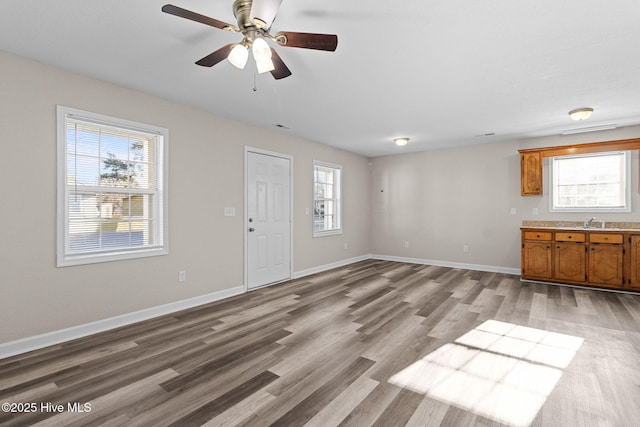 unfurnished living room with ceiling fan, sink, and light wood-type flooring