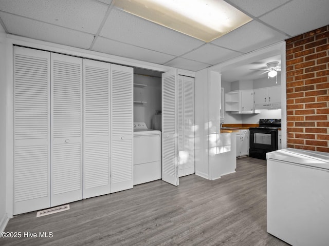 interior space featuring black electric range oven, white cabinetry, refrigerator, light hardwood / wood-style flooring, and washer / clothes dryer