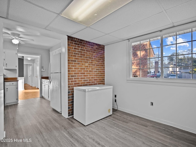 clothes washing area featuring ceiling fan, brick wall, and light hardwood / wood-style floors