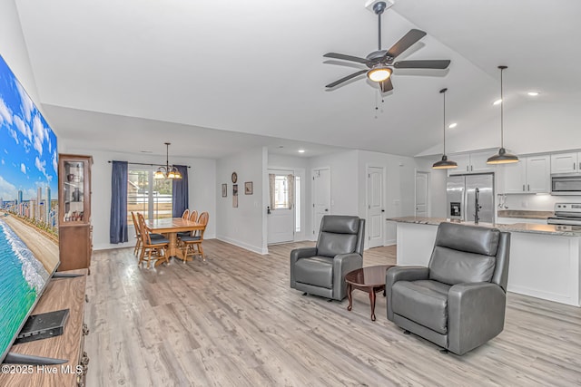 living room featuring lofted ceiling, ceiling fan with notable chandelier, and light hardwood / wood-style flooring