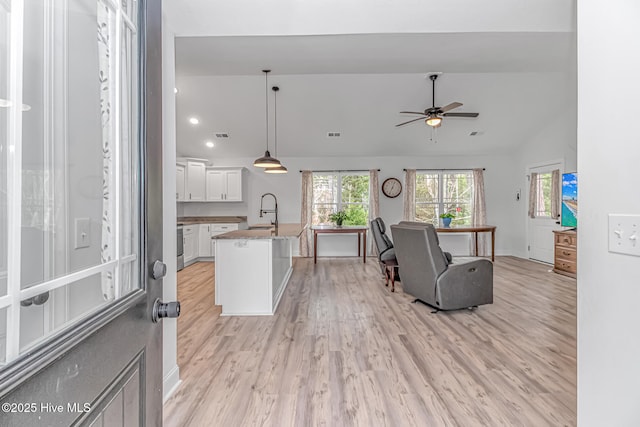 kitchen with pendant lighting, lofted ceiling, sink, white cabinets, and light hardwood / wood-style flooring