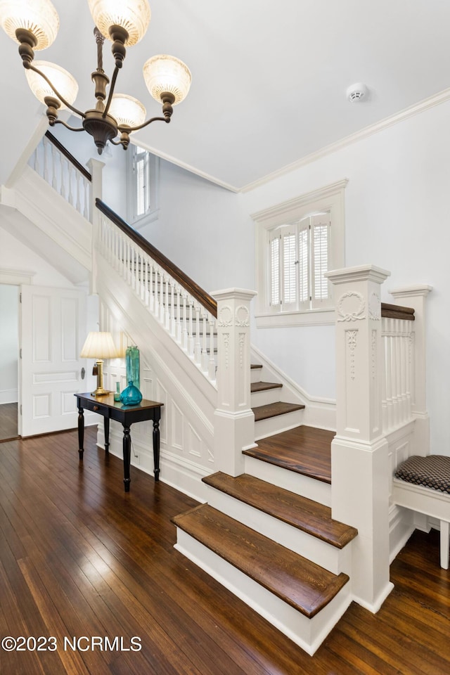 staircase with hardwood / wood-style flooring, crown molding, and a notable chandelier