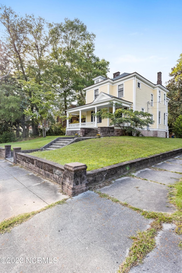 view of front of property featuring covered porch, a chimney, and a front yard