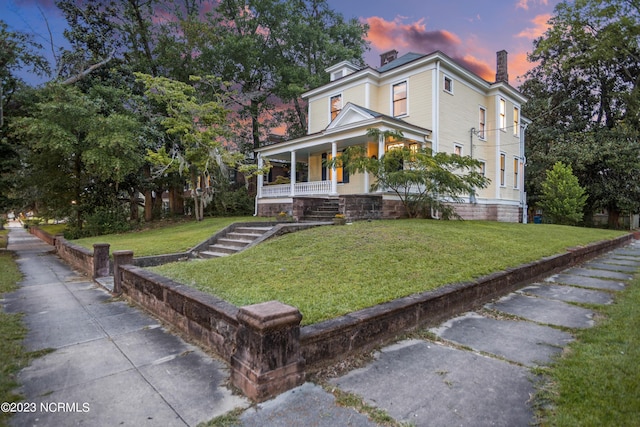 view of front facade featuring a porch, a yard, and a chimney