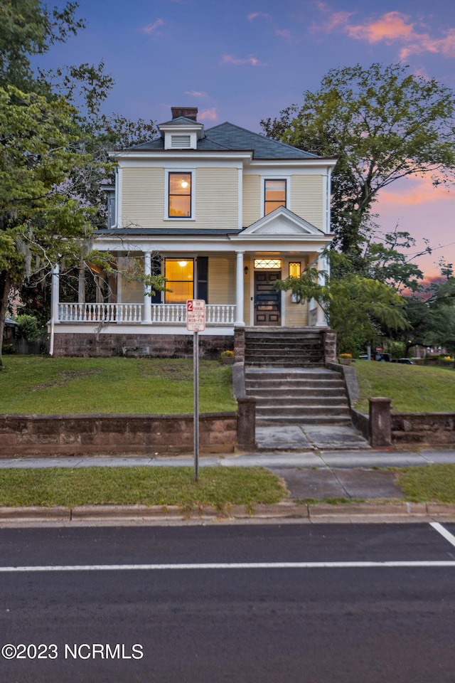 american foursquare style home featuring covered porch and a lawn
